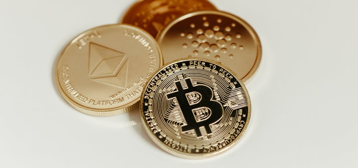 Close-up of Bitcoin, Ethereum, and Cardano coins on a plain background, showcasing digital currency.